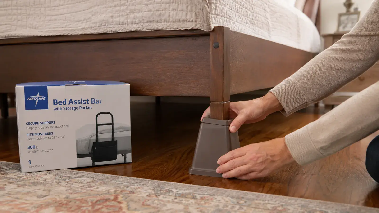Hand adjusting the height of a bed frame leg riser under a wooden bed, showing the gap between mattress and floor